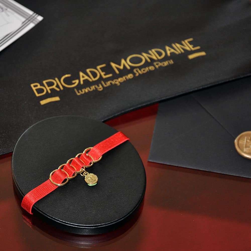 Здесь вы можете увидеть роскошный подарочный пакет от Brigade Mondaine. Внутри находится красный чокер с мешочком и подписанная специально для вас открытка. Все это находится в черном шелковом мешочке.