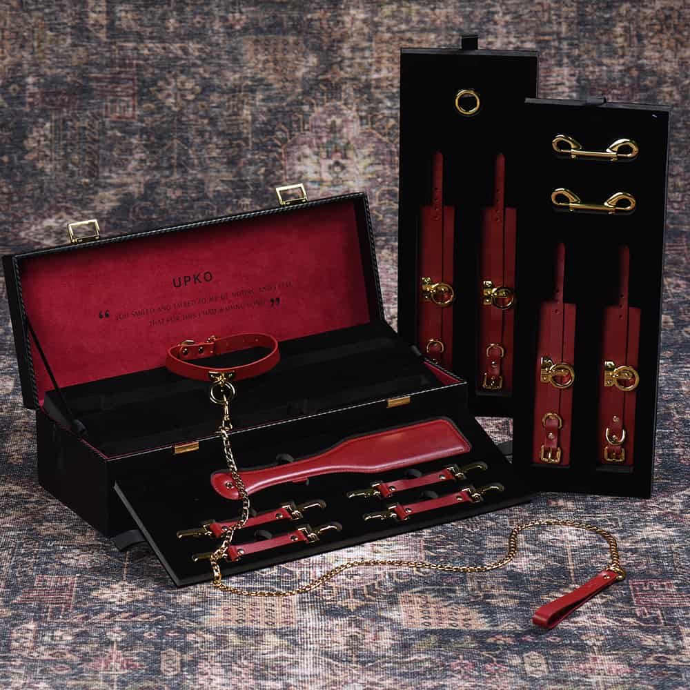 Tronco d' bondage de cuero rojo y accesorios BDSM incluyendo cuello, correa, esposas y paleta para azotar.