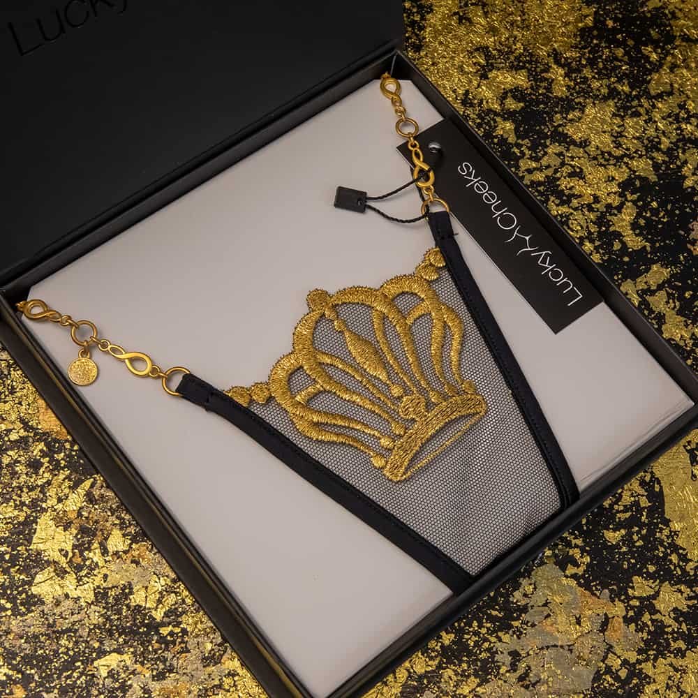 String Lucky Cheeks noir et or, la broderie suisse représente une couronne.De plus il possède un maintien fait d'une chaîne bijoux en Zamac doré.