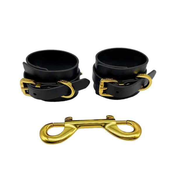 Handcuffs for wrists in black Italian leather with 24 carat gold-plated hooks in limited edition limited edition of the UPKO X Brigade Mondaine collaboration presented on a white background in HD at Brigade Mondaine