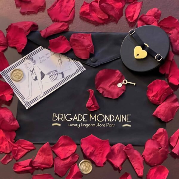 Embalaje negro de la brigada social. La tela lleva la inscripción de la brigada monda en oro. Acompañado de una tarjeta, una gargantilla negra y pétalos de rosa.