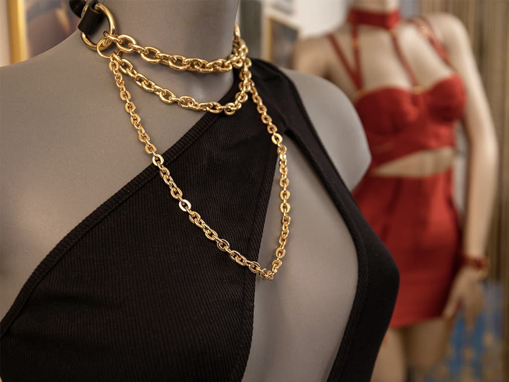 We can see a mannequin wearing an Elif Domanic bondage chocker in gold color. It has gold chains and a black leather strap on the neck.