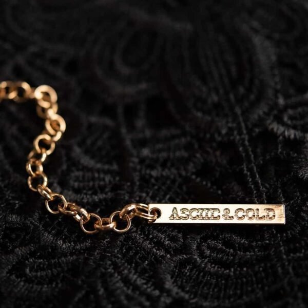 Ожерелье Alodie от бренда ASCHE & GOLD золотого цвета. Он изготовлен из кожи с тремя кольцами оружейного цвета, которые переплетаются между собой как центральное украшение.