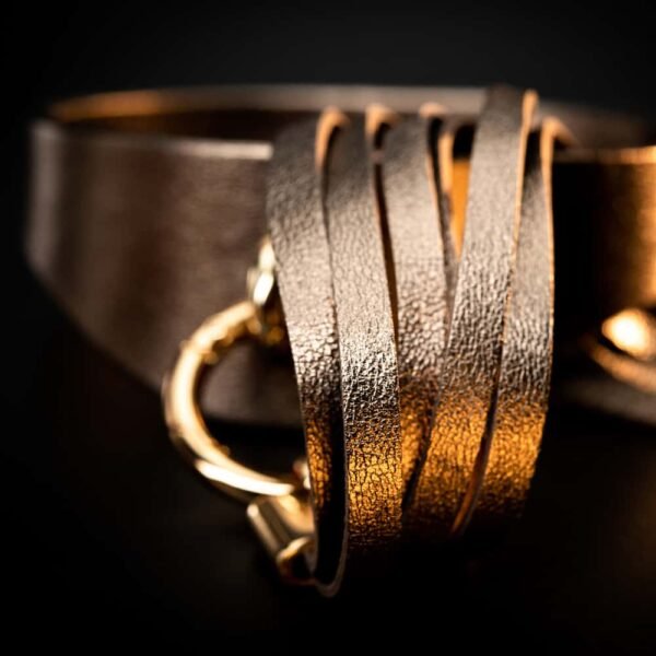 Ожерелье Ava от бренда ASCHE & GOLD цвета старого золота. Ожерелье имеет широкий вырез с кольцом в середине изделия. Это кольцо поддерживает большой помпон с кожаными лентами, идущими до пупка.